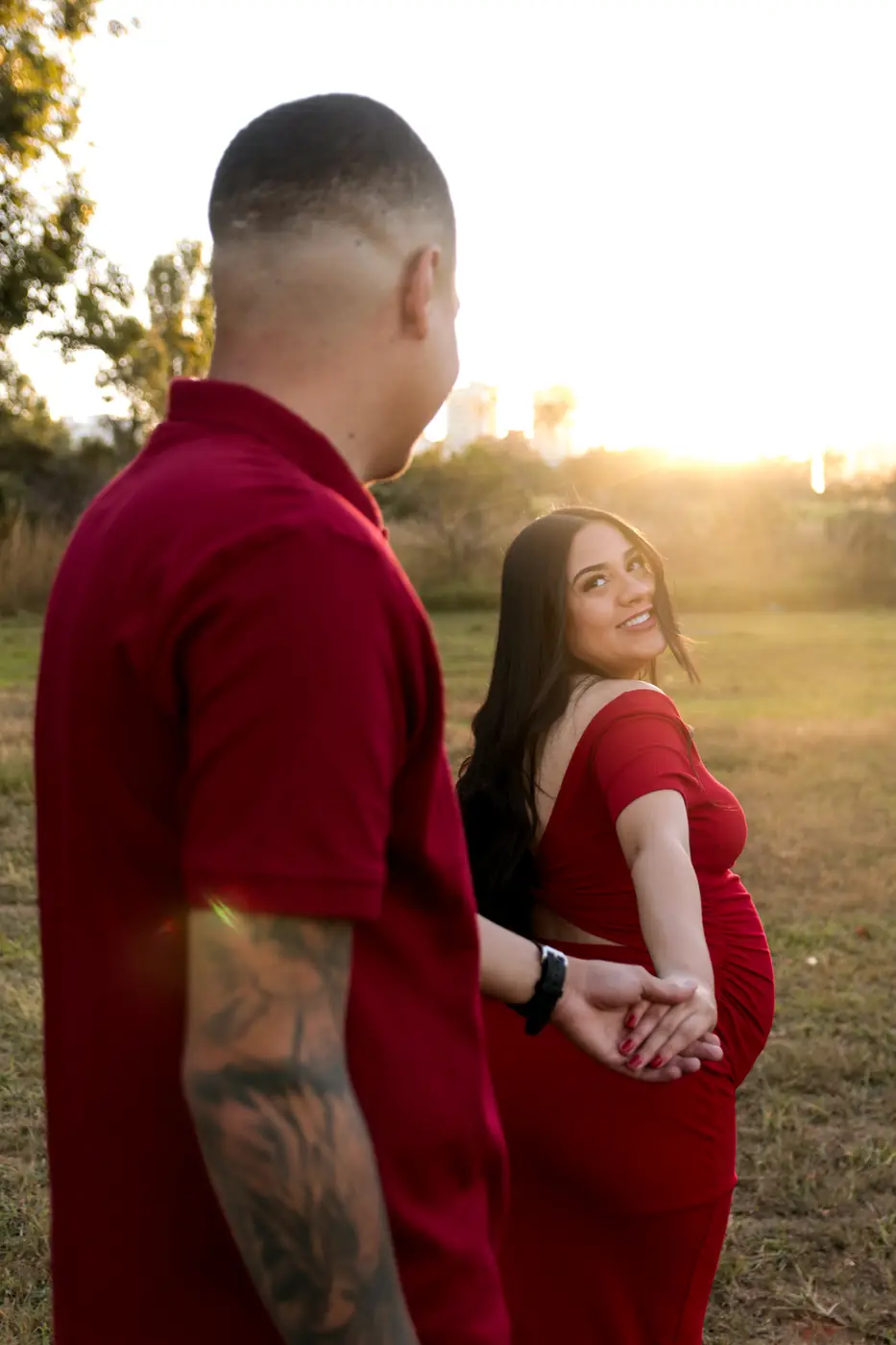 Casal ao pôr do sol, gestante de vestido vermelho